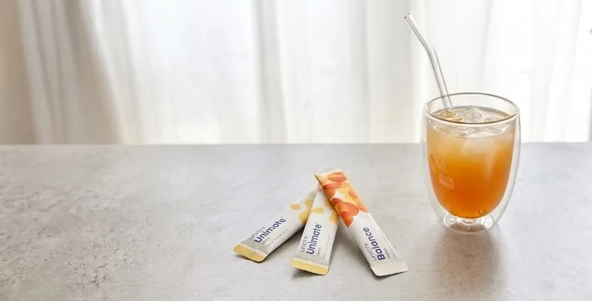 A glass of Unimate poured over ice, with Unimate and Balance stick packs beside it