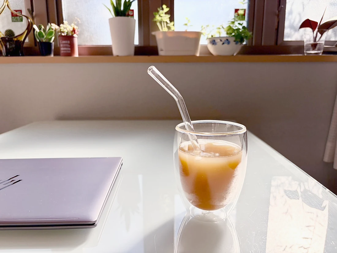 Un vaso de Unimate con hielo sobre un escritorio junto a la ventana, con una laptop al lado