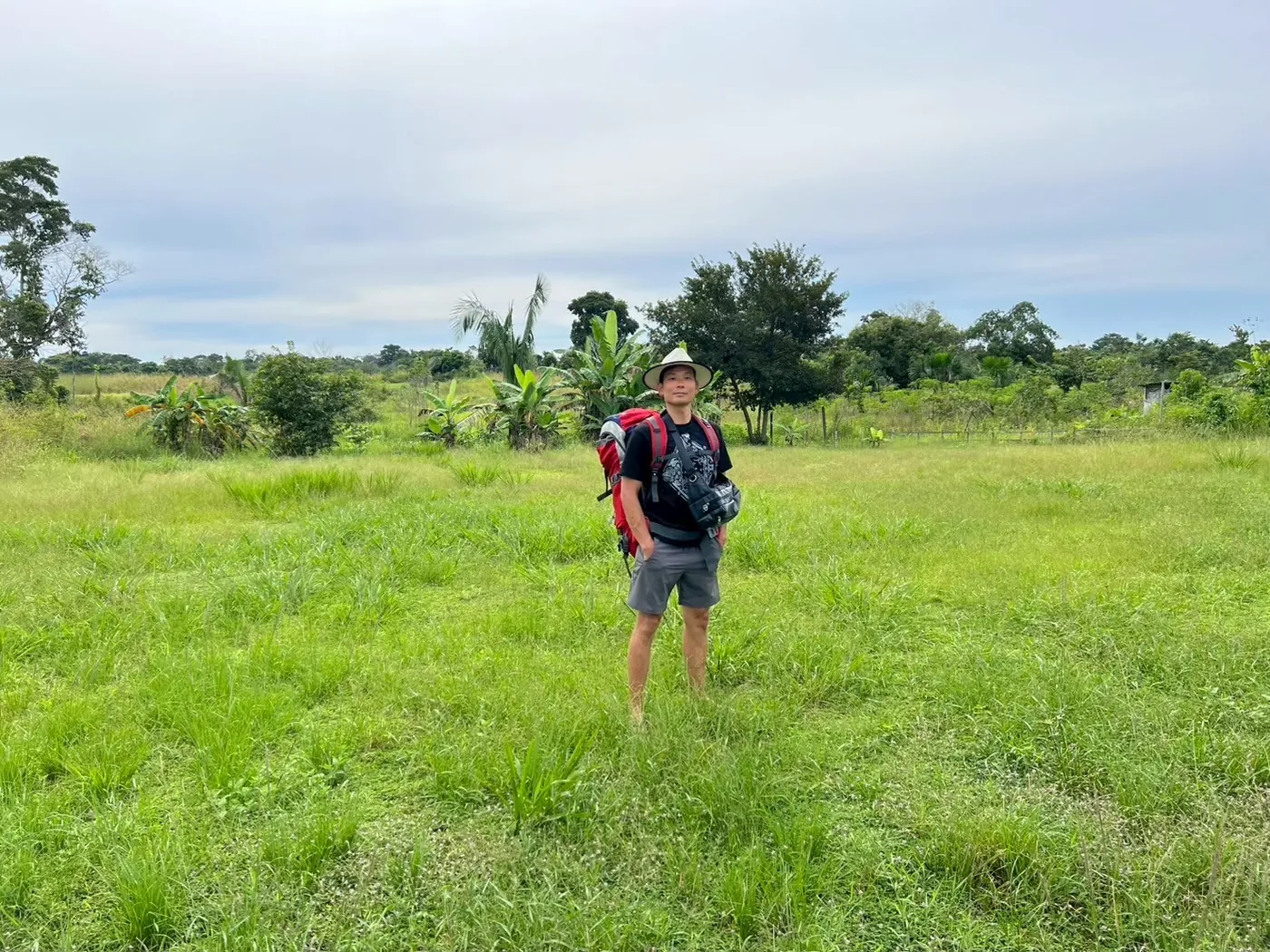 アマゾンの草地に、バックパックを背負い帽子をかぶった旅人が一人で立っている